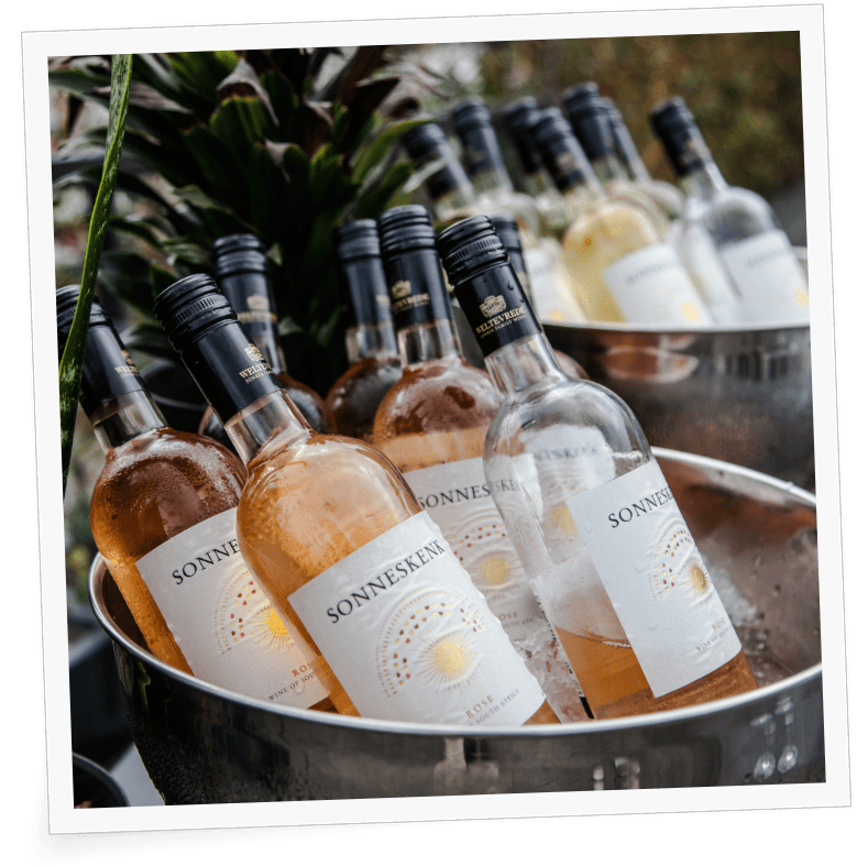 Ein mit Eis gefüllter Metalleimer enthält mehrere Flaschen Sonnenseklin-Wein mit einem sonnigen Blumenetikett, perfekt positioniert für eine Veranstaltung in einem Co-Working-Space. Die Flaschen sind mit metallischen An image from EDGE Workspaces.