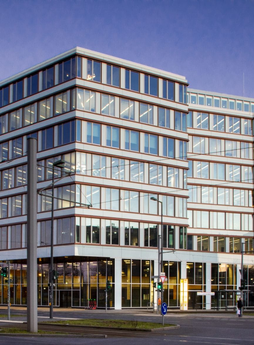 Modernes mehrstöckiges Bürogebäude mit einer Glasfassade, die einen klaren blauen Himmel reflektiert, mit sichtbaren Stützpfeilern und raumhohen Fenstern. Das Erdgeschoss ist über Fußgängerwege zum Eingang gut zugänglich. An image from EDGE Workspaces.
