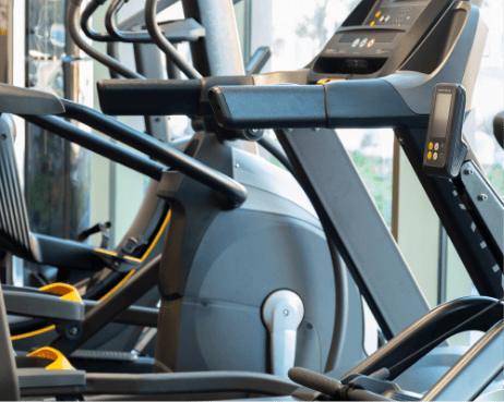Eine Reihe moderner Ellipsentrainer im Fitnessstudio eines Coworking-Space, ausgestattet mit digitalen Anzeigen und verstellbaren Griffen, vor einem sanft beleuchteten Hintergrund mit Reflexionen auf den glänzenden Metallkomponenten. An image from EDGE Workspaces.